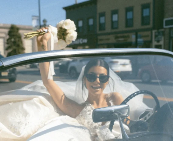 bride riding car and holding out white rose bouquet